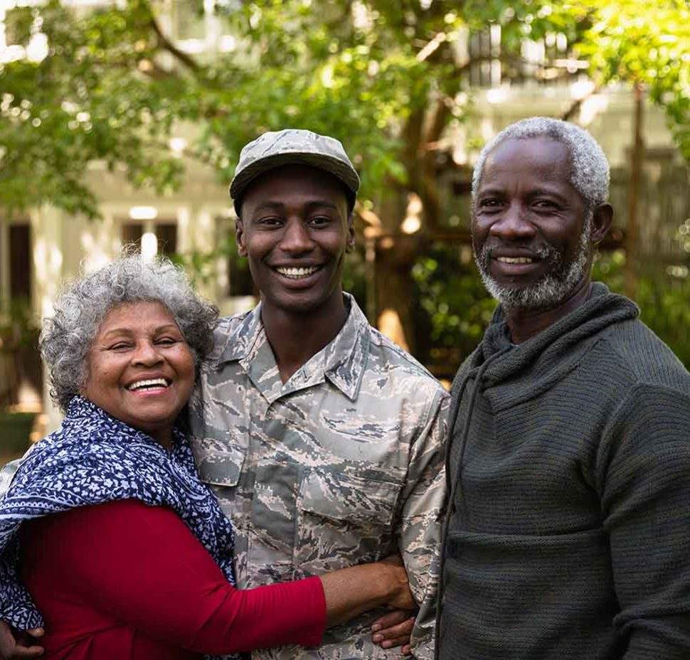 Young man in military uniform embracing family while outside and smiling for photo