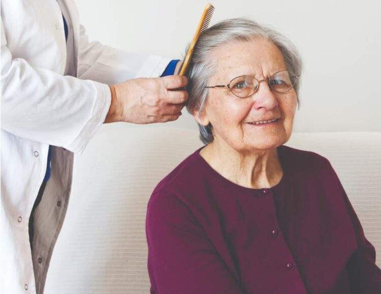 A senior woman sits while a caregiver brushes her hair