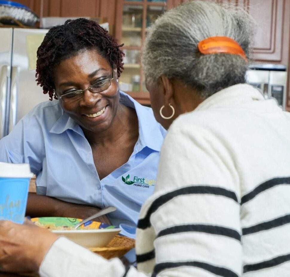 FirstLight Caregiver of the Year, Cynthia, sits with a client as she eats lunch