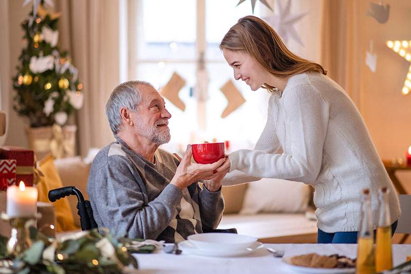 caregiving handing elderly man a red mug